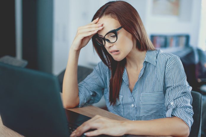 Frustrated young woman reading bad news on laptop screen